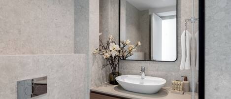Une salle de bain moderne avec un grand miroir, un lavabo blanc et un vase rempli de fleurs.