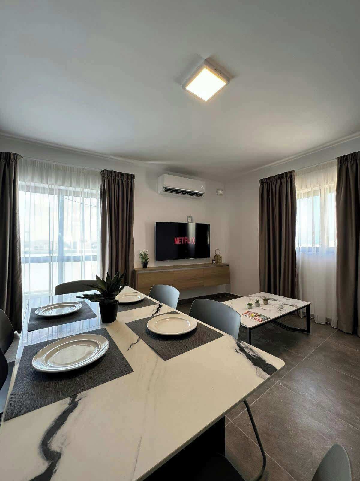 A modern dining area with a long table, chairs, and a flat-screen TV displaying 'NETFLIX'.