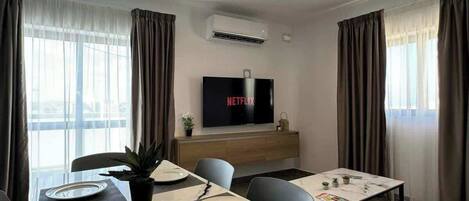 A modern dining area with a long table, chairs, and a flat-screen TV displaying 'NETFLIX'.