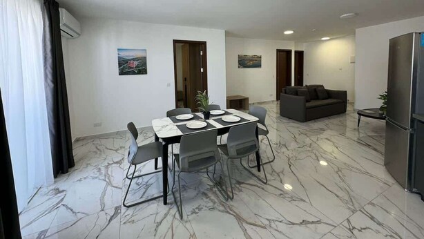 Un salon moderne avec un coin repas, un sol en marbre et un canapé gris.
