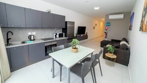 Una cocina moderna con armarios grises, una mesa de comedor con sillas, una mesita redonda con una planta y un sofá gris en la sala.
