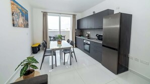 Una cocina moderna con un refrigerador de acero inoxidable, una mesa de comedor con sillas y un ventanal con cortinas.