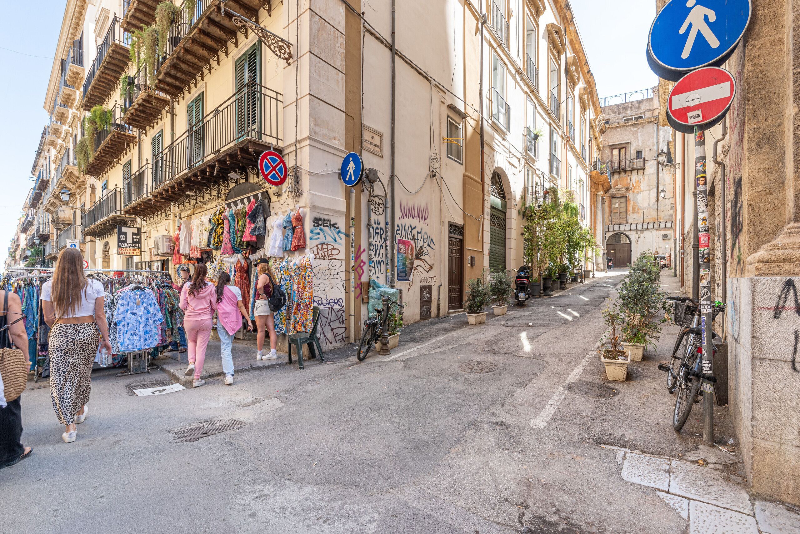 Une rue avec des piétons, un vélo et un immeuble doté de balcons et orné de graffitis.