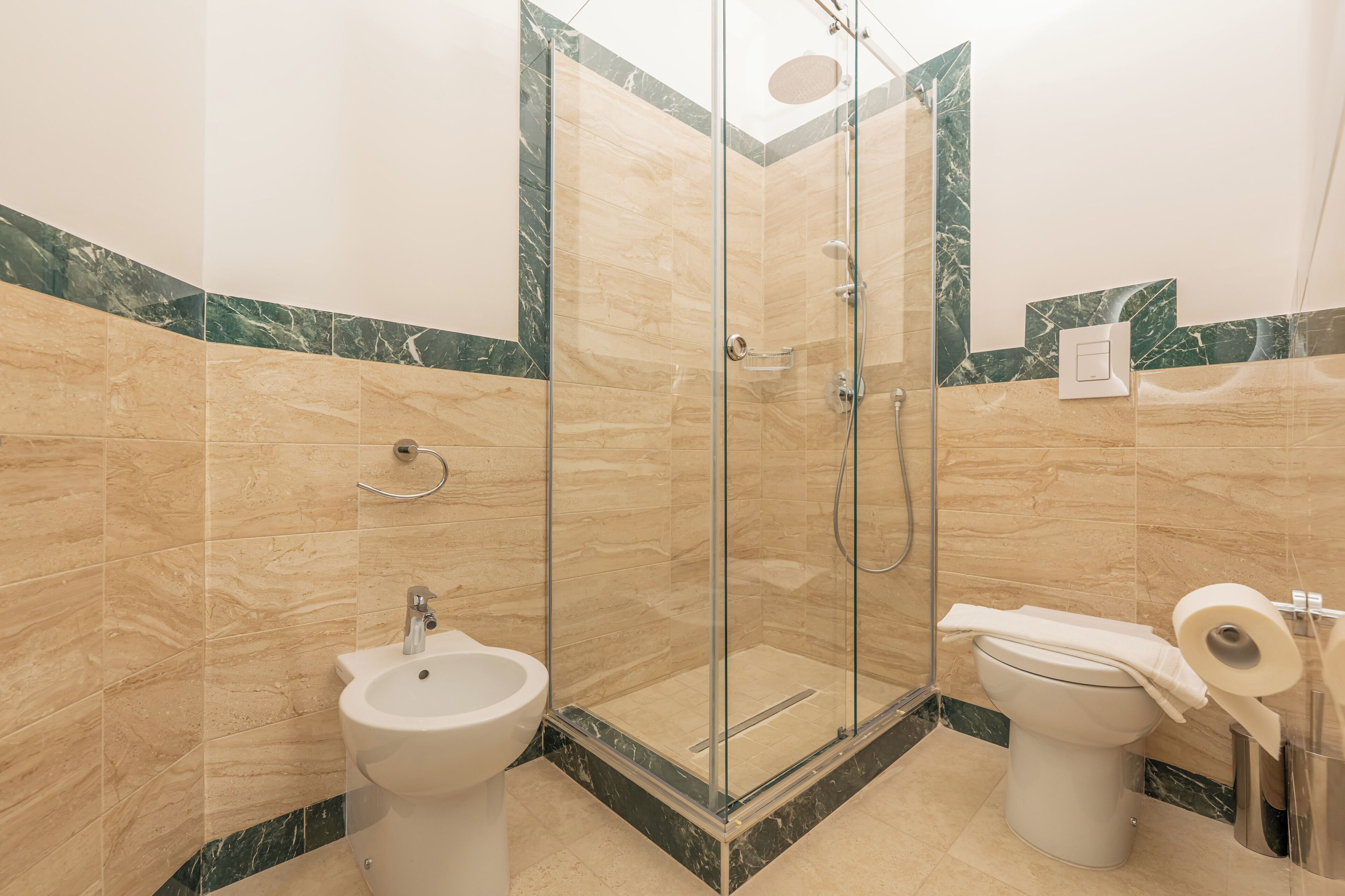 Une salle de bain dotée d’une douche à parois de verre, d’un bidet et de toilettes avec une serviette et du papier toilette à disposition.