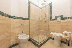 A bathroom with a glass-enclosed shower, a bidet, and a toilet with a towel and toilet paper. - Molo Angioino Suites (Naples)