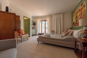 A spacious bedroom with a large bed, a sitting area with a chair, a small table, and a view of the outside through a glass door. - Molo Angioino Suites (Naples)