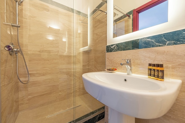 A modern bathroom with a glass-enclosed shower, a white sink, and marble tiles. - Molo Angioino Suites (Naples)