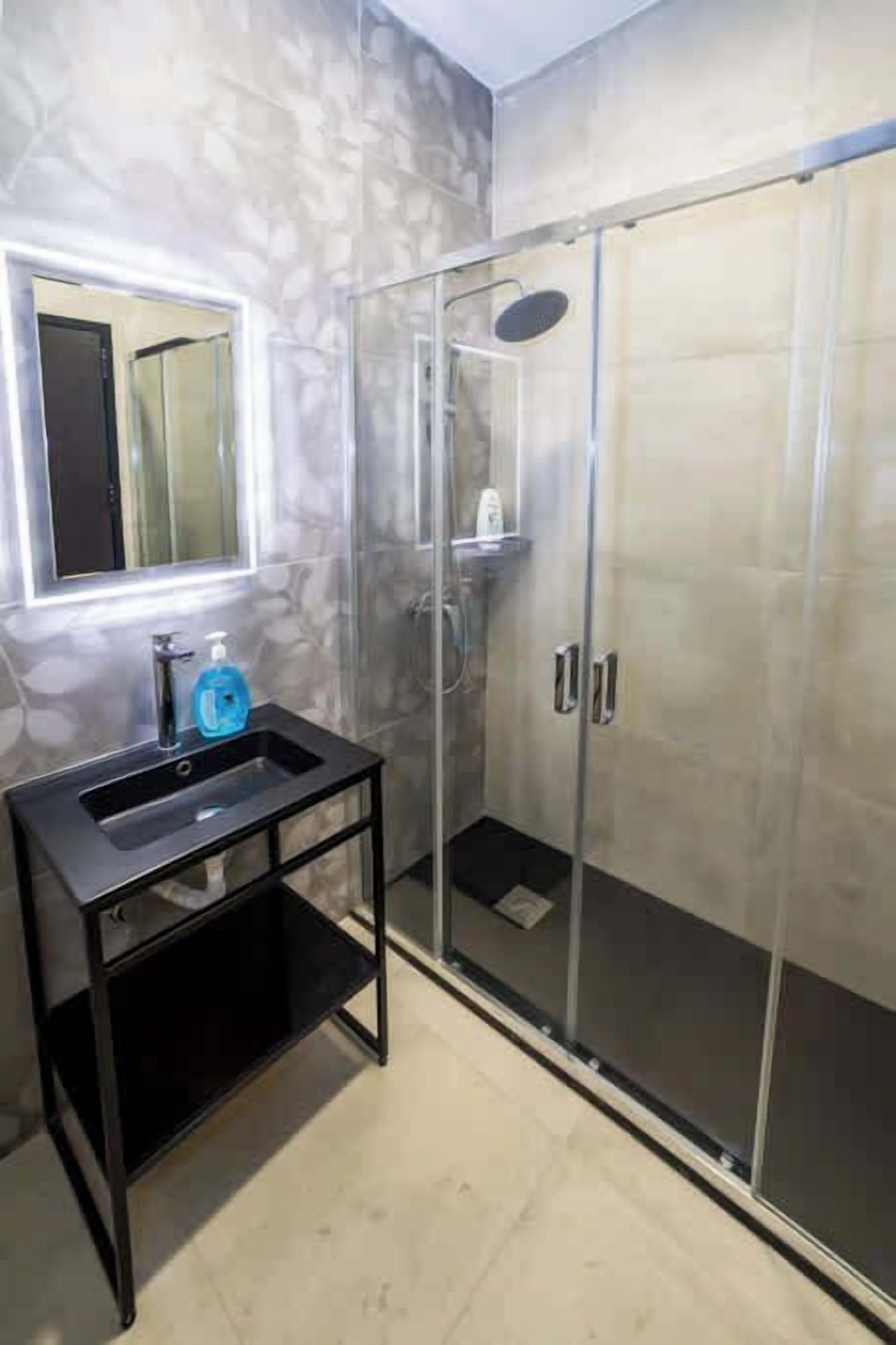 Une salle de bain avec une douche à parois de verre, un lavabo noir avec un miroir et un sol carrelé.