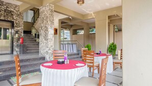 A covered outdoor dining area with round tables, chairs, and a staircase leading to an upper level. - Treebo Sunrise Apartments (Pune)