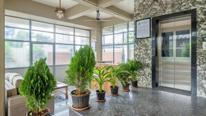 A lobby with large windows, a reception desk, and several potted plants. - Treebo Sunrise Apartments (Pune)