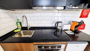 Een kleine keuken met een rvs spoelbak, een koffiezetapparaat, een waterkoker en een kleine koelkast.