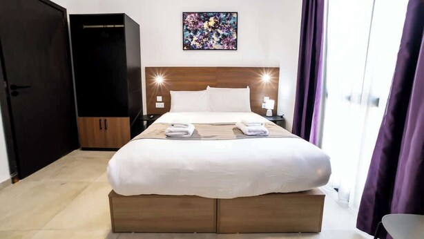 Een hotelkamer met een groot bed, een houten hoofdbord, twee nachtkastjes met lampen, een schilderij aan de muur en een garderobe.