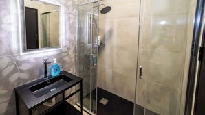Een moderne badkamer met een glazen douchecabine, een wastafel met spiegel en een zeepdispenser.