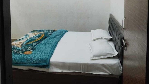 A small, neatly made bed with a patterned blanket and white pillows in a room with a wooden wardrobe and a ceiling fan. - HOTEL K K PALACE (Khatoo)