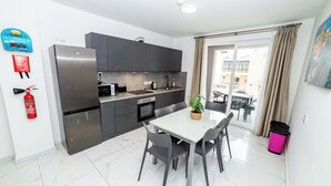 Une cuisine moderne dotée d’un réfrigérateur en acier inoxydable, de meubles de couleur sombre et d’un coin repas avec une table et des chaises blanches.