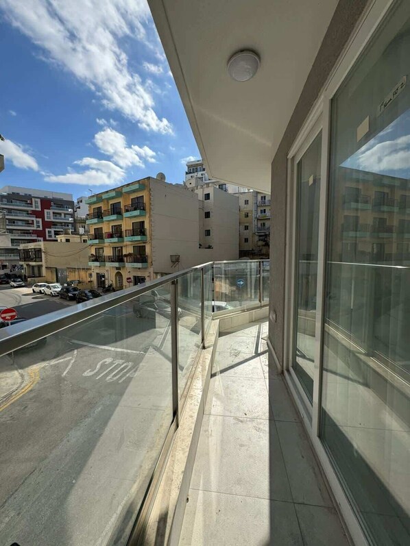A balcony with a glass railing overlooking a street with parked cars and buildings.