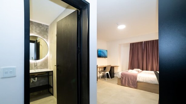 Habitación de hotel con cama, escritorio, silla, televisor y baño con espejo y lavabo.
