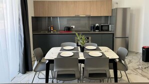 A modern kitchen with wooden cabinets, a stainless steel refrigerator, and a dining area with a marble table and chairs. - Modern 1-Bedroom Apartment with Balcony – by HostMT (San Pawl il-Baħar)