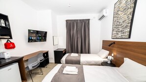 Habitación de hotel con dos camas, un escritorio, una silla, un televisor y una cortina.
