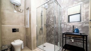 Un baño moderno con ducha de vidrio, inodoro y lavamanos con espejo.