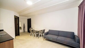 Una sala de estar moderna con un sofá gris, una mesa de comedor con sillas y una zona de cocina.
