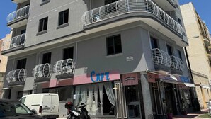 Un edificio de varios pisos con balcones, una cafetería en la planta baja y una furgoneta estacionada en la parte delantera.