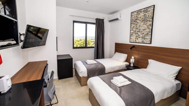 Habitación de hotel con dos camas, un escritorio, una silla, un televisor y una ventana con vistas.
