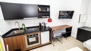 Cocina compacta con encimera negra, electrodomésticos de acero inoxidable, un refrigerador pequeño y una mesa de comedor de madera con dos sillas.