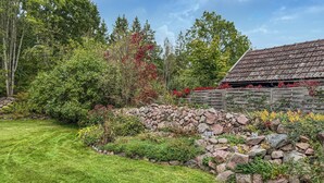 Un mur de pierres avec une clôture en bois, une pelouse bien entretenue et un bâtiment doté d’un toit en tuiles.