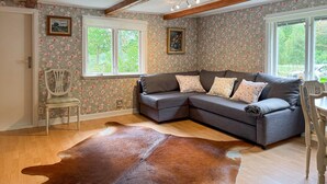 Un salon chaleureux avec un canapé d’angle, un papier peint à motifs floraux et un grand tapis en cuir.