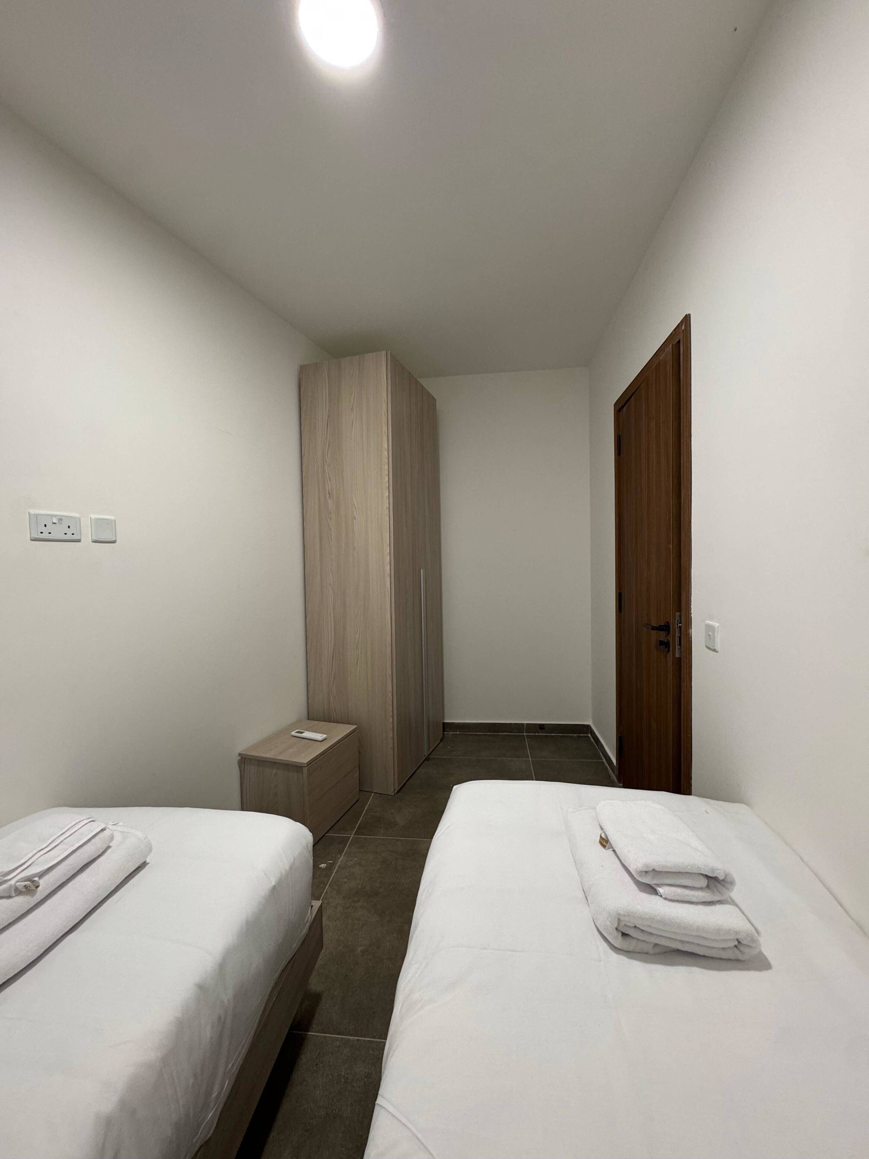 Une chambre d’hôtel avec deux lits, une armoire, une table de chevet et une porte.