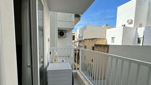 Un balcon étroit avec une balustrade blanche, une petite table et une bouteille d’eau.