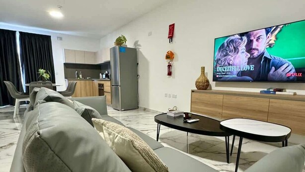 Un salon moderne avec un canapé gris, une table basse et un téléviseur à écran plat diffusant un film.