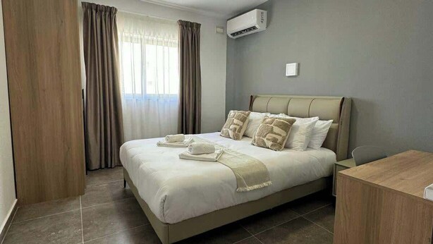 Une chambre d’hôtel moderne avec un grand lit, un bureau et un climatiseur fixé au mur.
