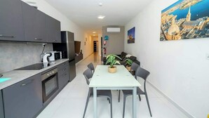 Una cocina moderna con gabinetes oscuros, una encimera blanca y un comedor con mesa y sillas. En la pared, hay un cuadro de un paisaje urbano.