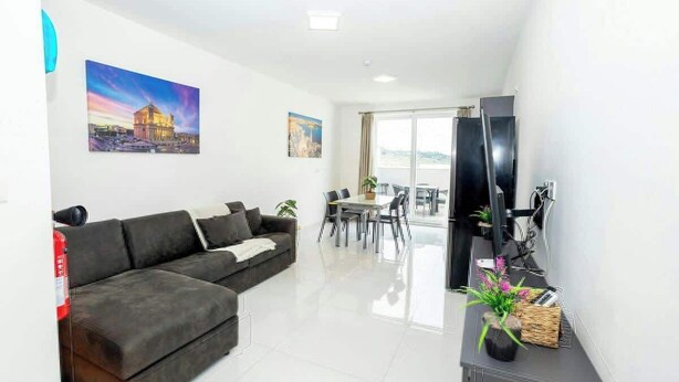 Una sala de estar moderna con un sofá seccional, una mesa de comedor con sillas, un televisor de pantalla plana y un balcón con vistas.