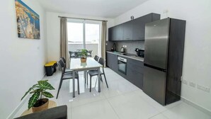 Una cocina moderna con un refrigerador de acero inoxidable, una mesa de comedor con sillas y una ventana con cortinas.