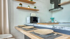 A modern kitchen with a built-in microwave, wooden shelves with plants, and a marble countertop. - Residence at Damara Village Jimbaran (Bali)