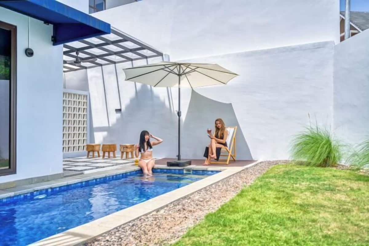 A swimming pool with two people, a pergola, and a large umbrella.