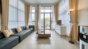 A modern living room with a black leather sofa, a glass coffee table, and a white desk. - Residence at Damara Village Jimbaran (Bali)