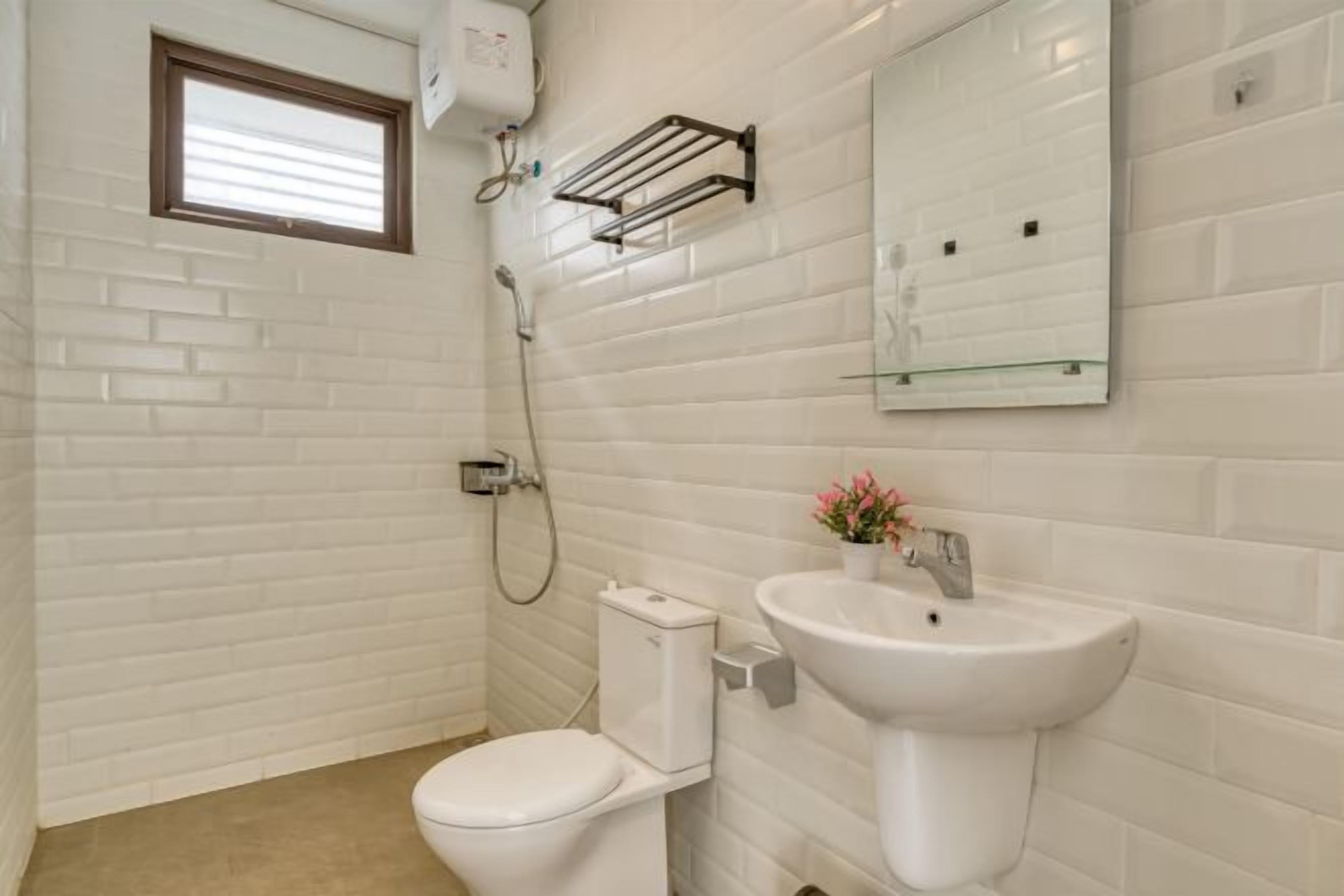 Een badkamer met witte betegelde wanden, een toilet, een wastafel, een douche en een raam.