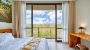 A hotel room with a bed, a desk, a chair, and a large window with a view of the outdoors. - Residence at Damara Village Jimbaran (Bali)