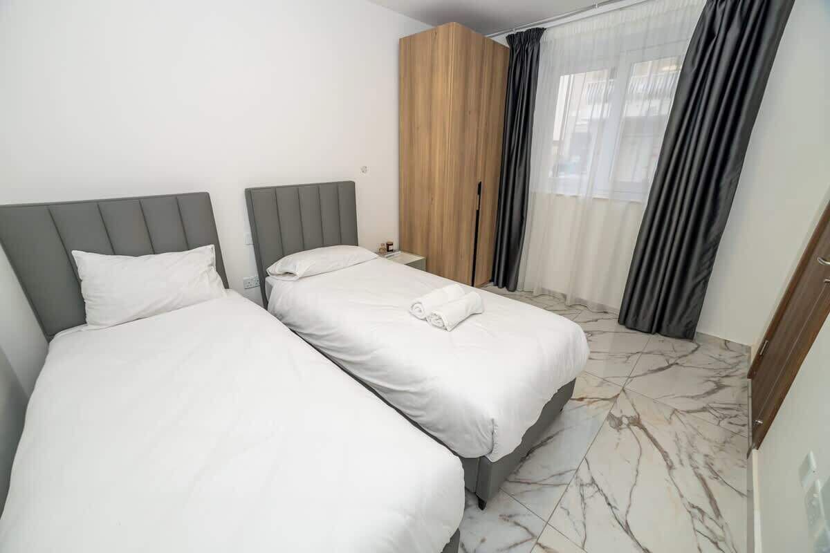 A hotel room with two beds, a wooden wardrobe, a nightstand, and a window with curtains.