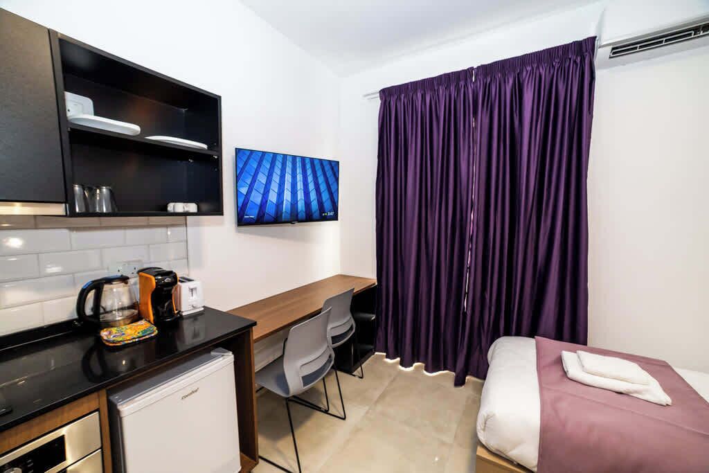 A compact hotel room with a kitchenette, a bed, a desk, and a TV.