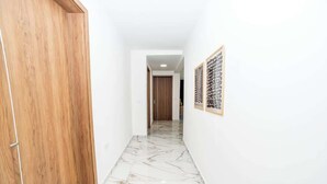 Ein Korridor mit einer Holztür links, einem Marmorboden und gerahmten Kunstwerken an der rechten Wand.