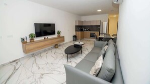 A modern living room with a grey sofa, a flat-screen TV, and a marble floor. - Luxury 3-Bedroom Family Maisonette – by HostMT (San Pawl il-Baħar)