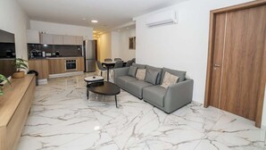 A modern living room with a grey sofa, a coffee table, and a kitchen in the background. - Luxury 3-Bedroom Family Maisonette – by HostMT (San Pawl il-Baħar)