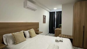 Habitación de hotel con una cama grande, cabecera de madera, mesita de noche, escritorio, armario y unidad de aire acondicionado en la pared.