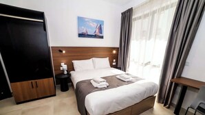 Habitación de hotel con cama, mesita de noche, escritorio, silla, armario y un cuadro en la pared.