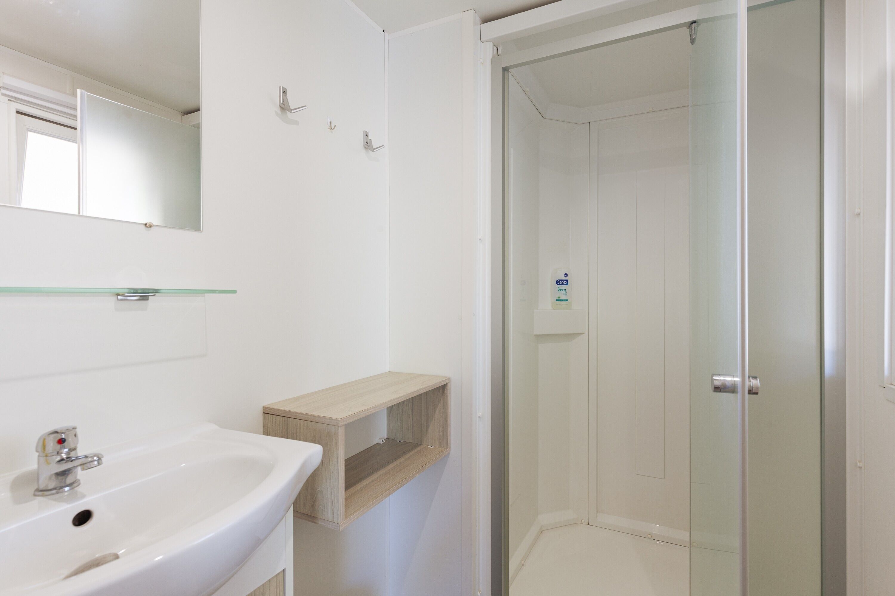 A bathroom with a white sink, mirror, and glass shower enclosure.